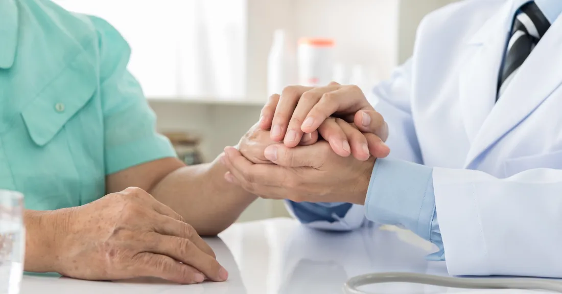 Médico sosteniendo las manos de un paciente en consulta
